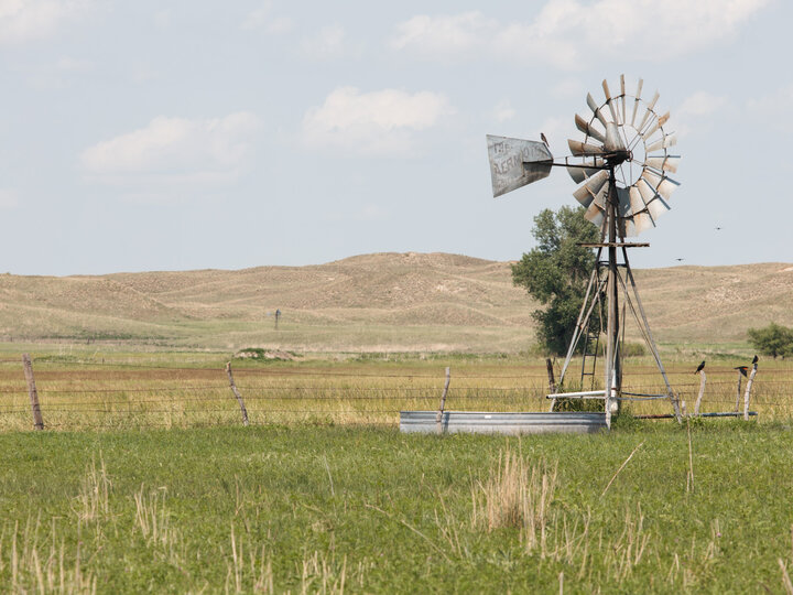 Windmill in a grassy field with rolling hills and a clear sky.